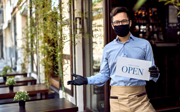 man wearing mask holding Open sign in restaurant entrance