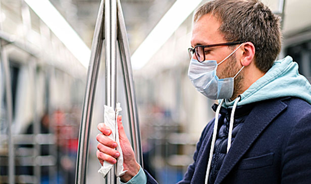 man on subway wearing mask, holding rail with napkin