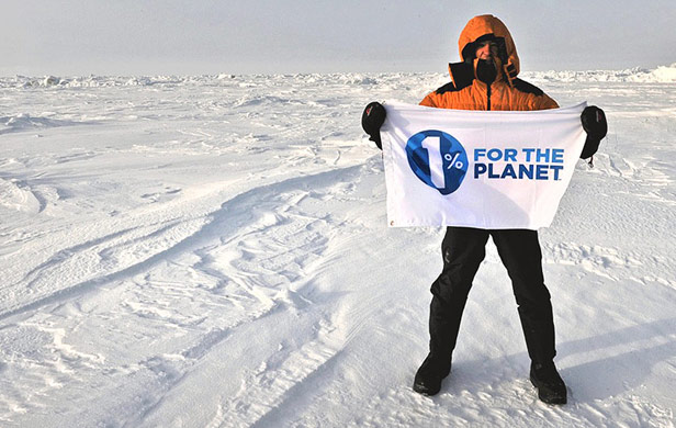 Man standing on snowy ground holding "1% For The Planet" sign