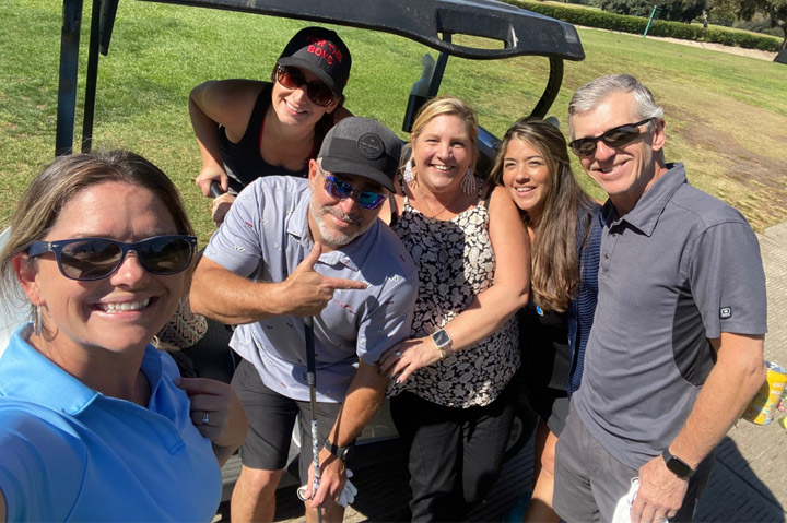 group of men and women standing together in front of golf cart