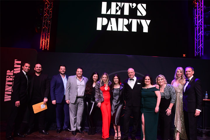 group of people at awards ceremony standing under a Let's Party sign