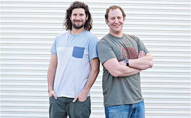 two men standing shoulder-to-shoulder against metal wall