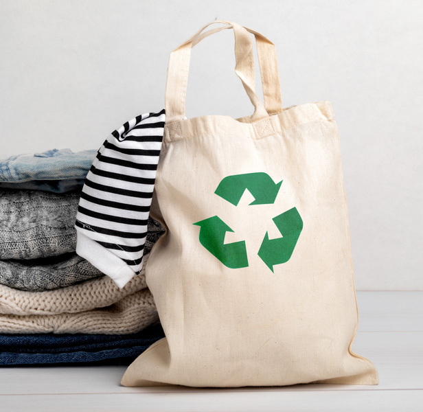 tote bag with recycle logo on front, next to stack of clothing