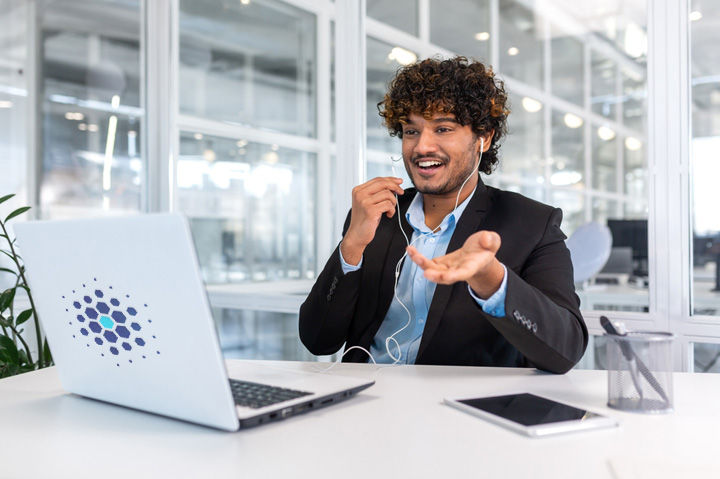 man talking on phone with headphones, sitting in front of laptop